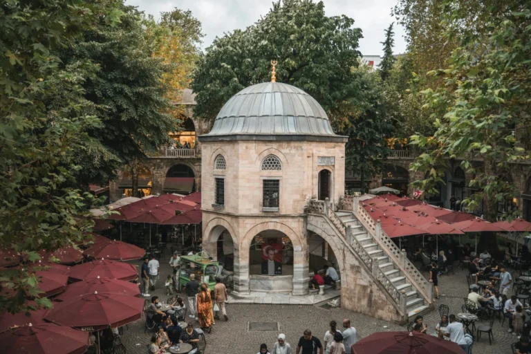 Koza Han courtyard in Bursa, Turkey, filled with people, red umbrellas, and historic Ottoman architecture.