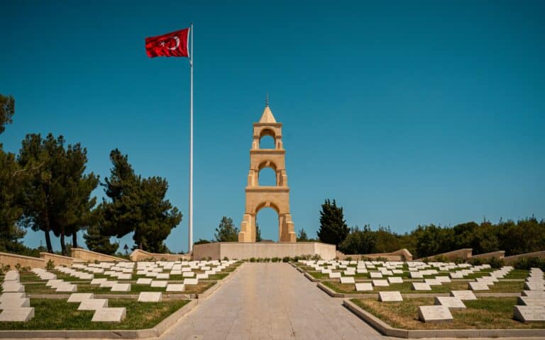 Gallipoli Martyrs Memorial with Turkish flag in Çanakkale, Turkey – historic site from World War I surrounded by gravestones and pine trees.