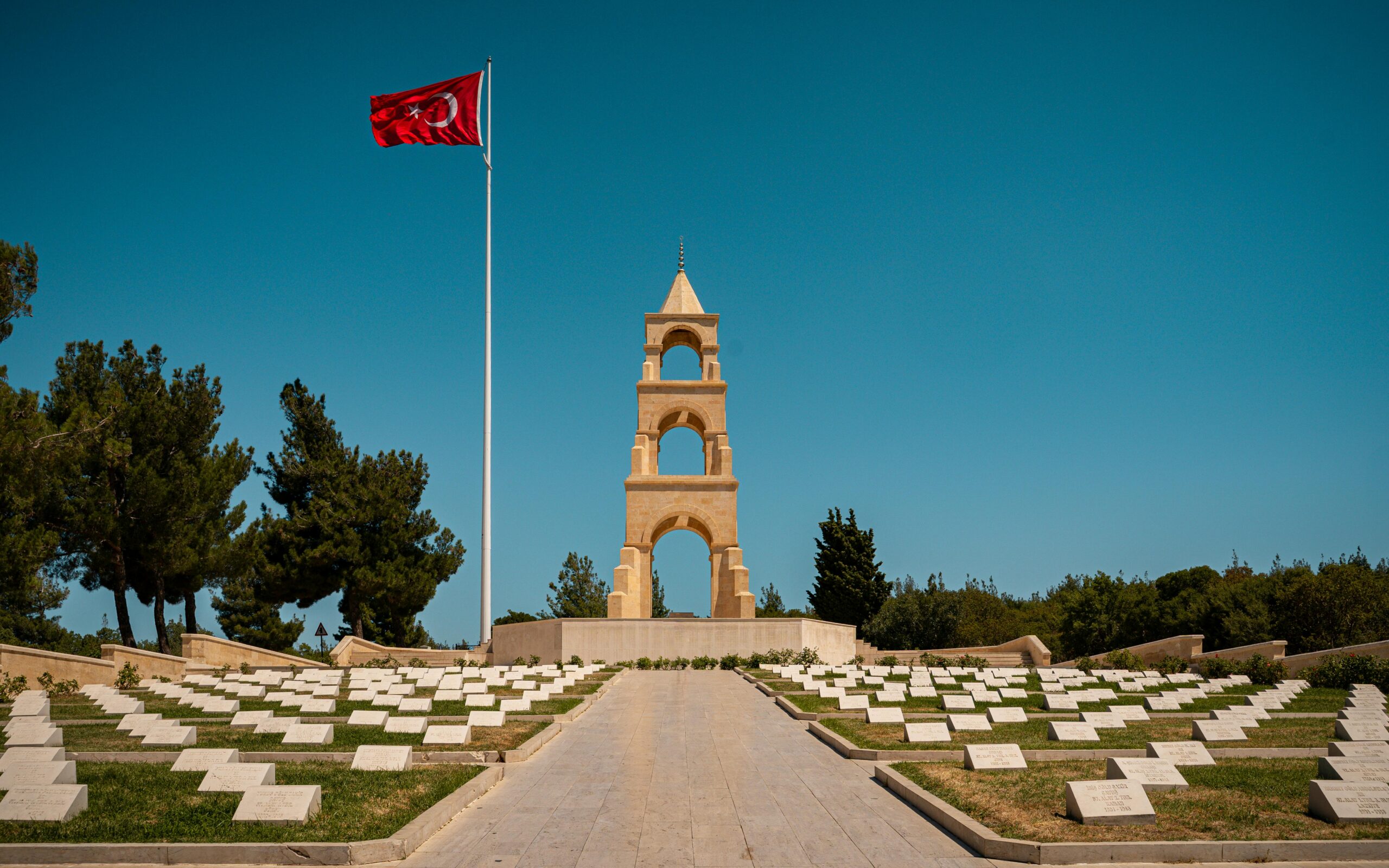 Gallipoli Martyrs Memorial with Turkish flag in Çanakkale, Turkey – historic site from World War I surrounded by gravestones and pine trees.
