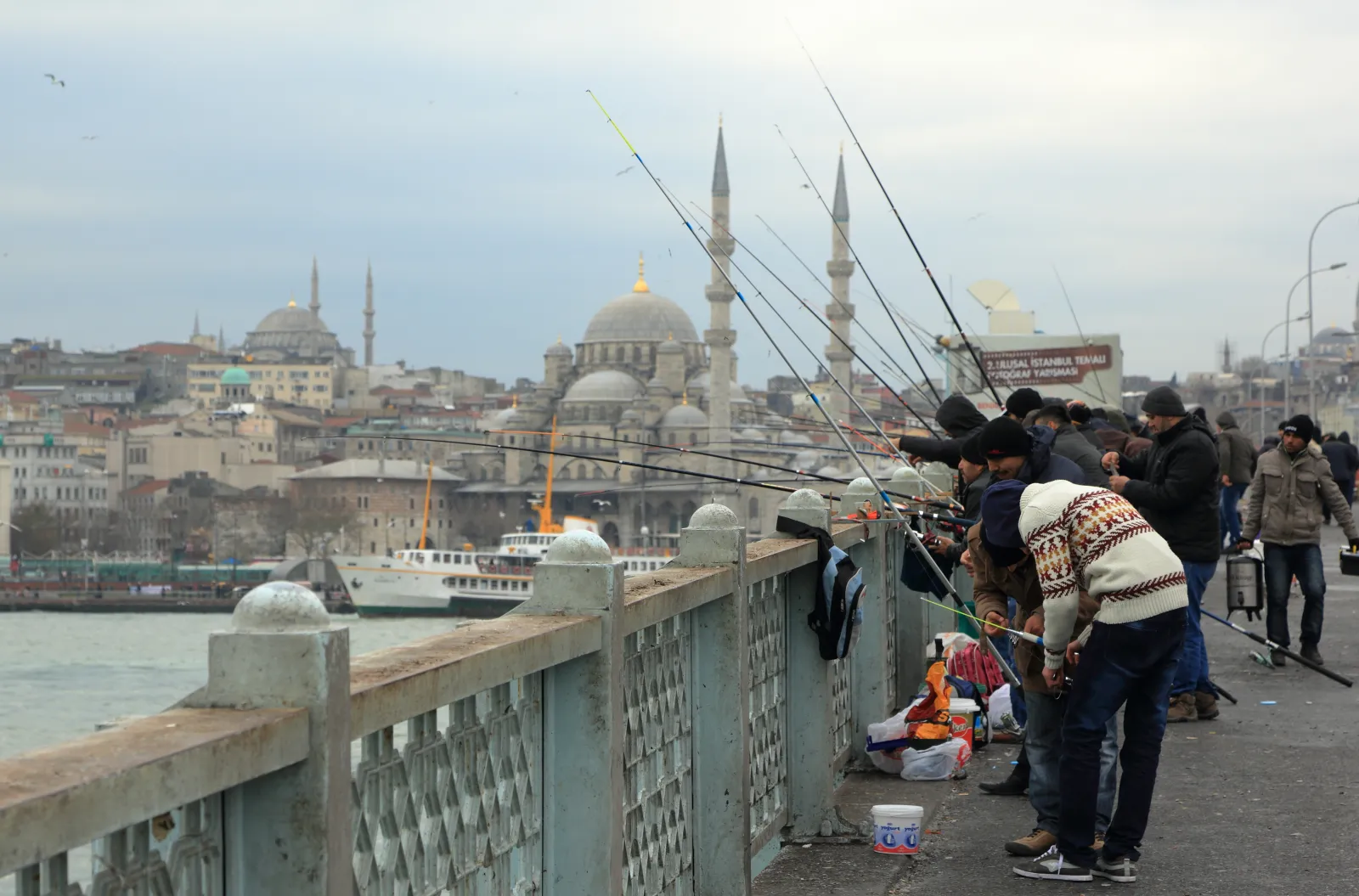 Fishermen lining the upper deck of Galata Bridge over the Golden Horn at sunset in Istanbul