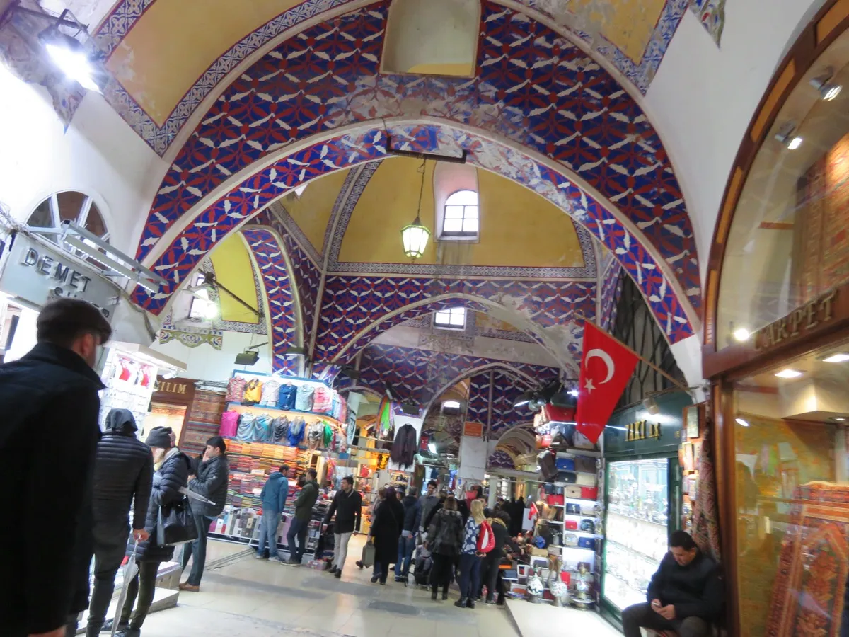 Painted vaulted ceiling and arched corridor inside the Grand Bazaar with shops and visitors