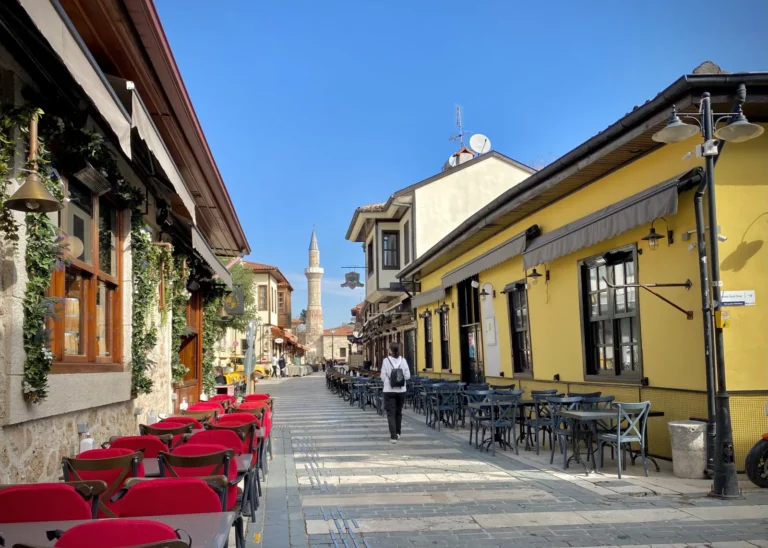 Narrow cobblestone street in Kaleici Antalya with Ottoman houses, bougainvillea, and a minaret visible in the background