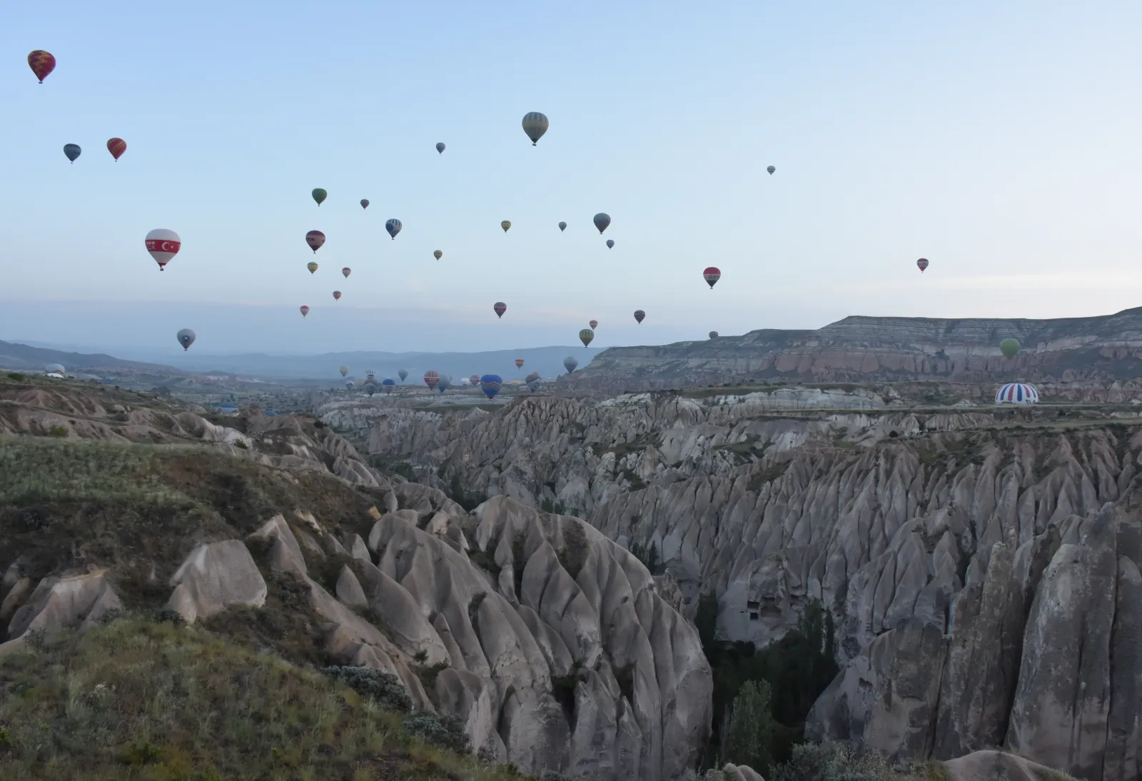 Hot air balloons floating over the fairy chimney formations of Love Valley in Cappadocia at sunrise