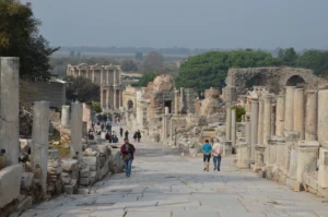 Visitors walking along the marble-paved Curetes Street in Ephesus with ruined columns and monuments on both sides