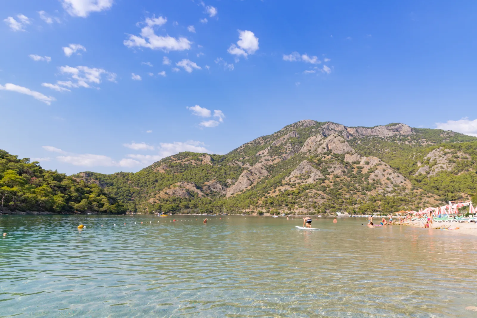 Swimmers in the calm, shallow turquoise water of the Oludeniz Blue Lagoon with pebble beach