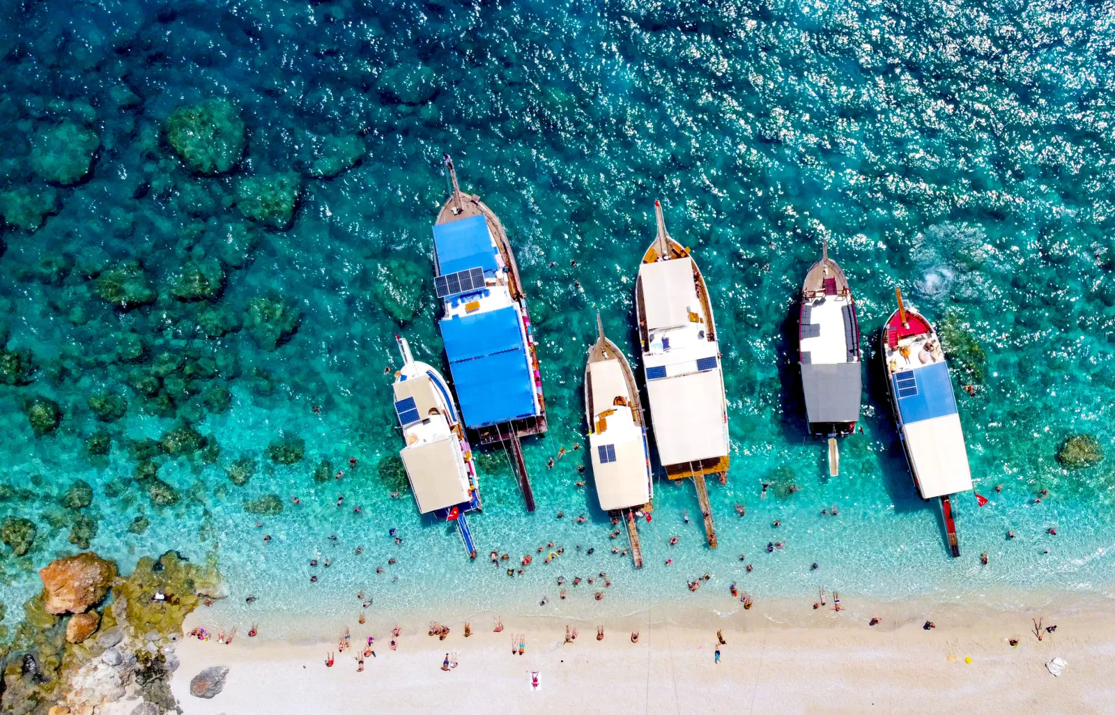 A cove at Suluada Island with white sand beach and clear turquoise water, boats anchored offshore